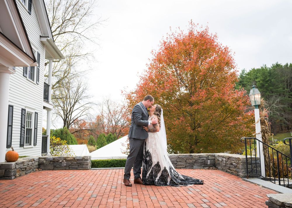 Autumn trees with vibrant orange foliage frame a brick patio and white house exterior in a residential setting.