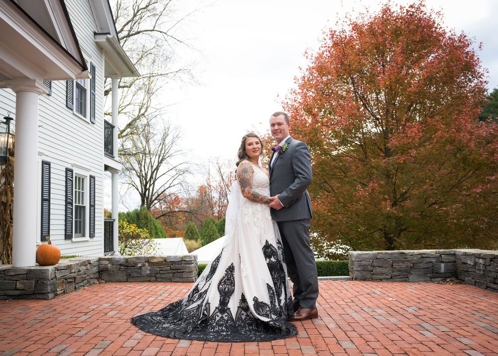 A wedding couple poses for photos on a brick patio surrounded by autumn foliage.