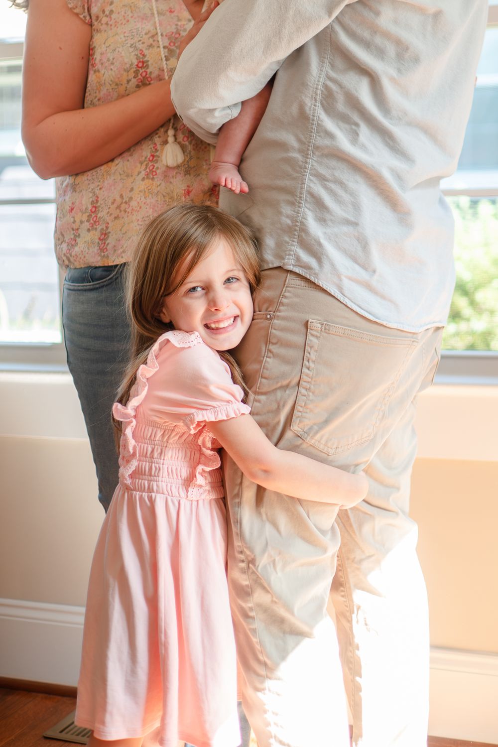 A child in a pink dress hugs someone wearing white clothing in a bright indoor setting.