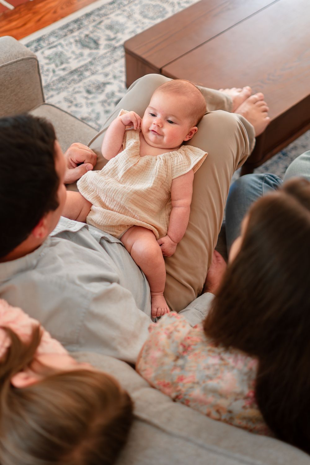 A baby in a cream-colored outfit lies on a couch between two adults in a series of candid family photos.