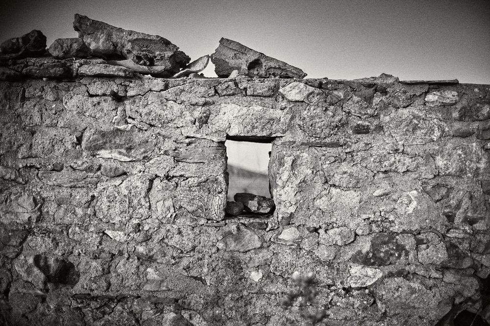 Long weathered stone wall with rough texture and small openings photographed in black and white.