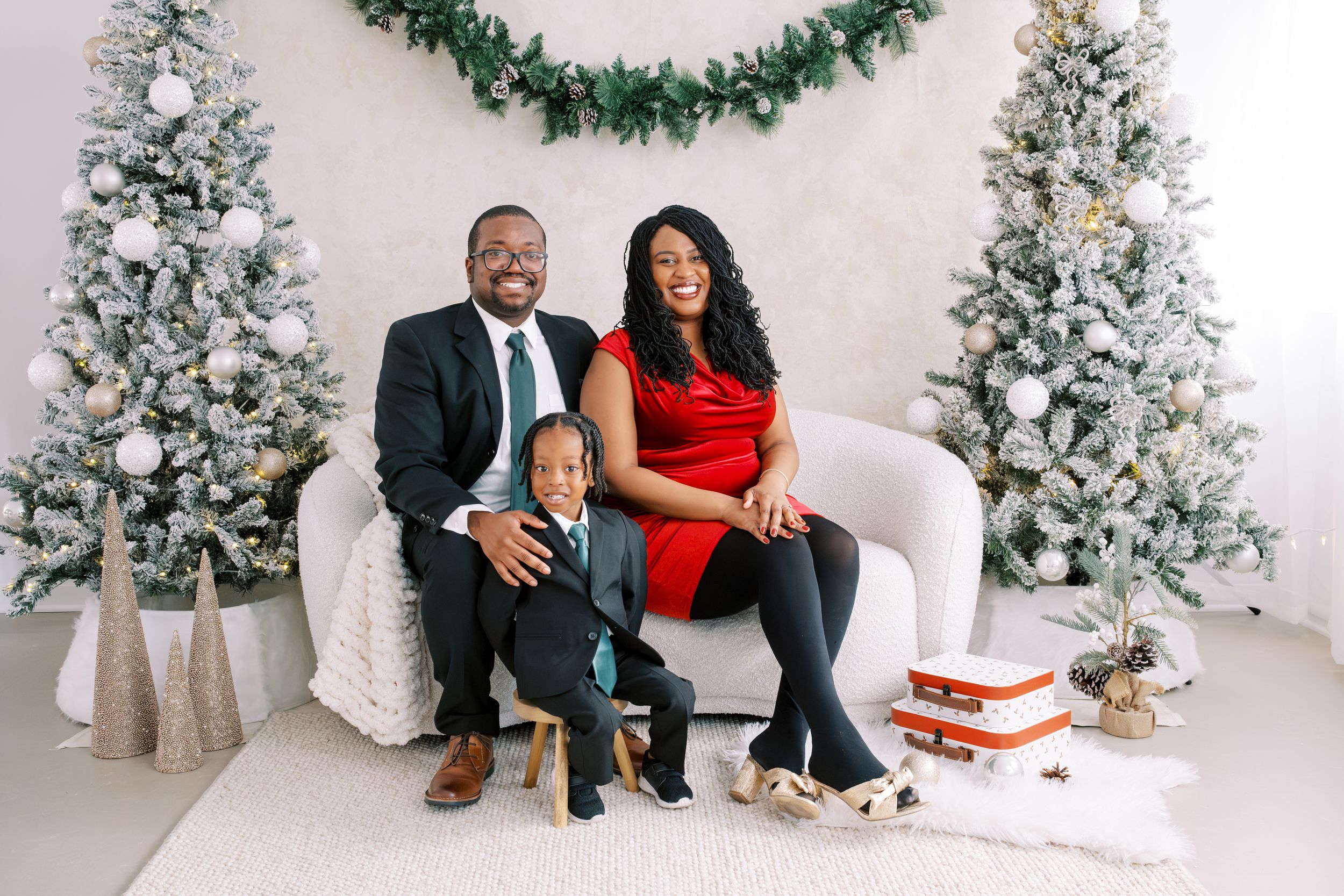 A festive holiday photoshoot setup with snow-covered Christmas trees and a white couch against a white backdrop.