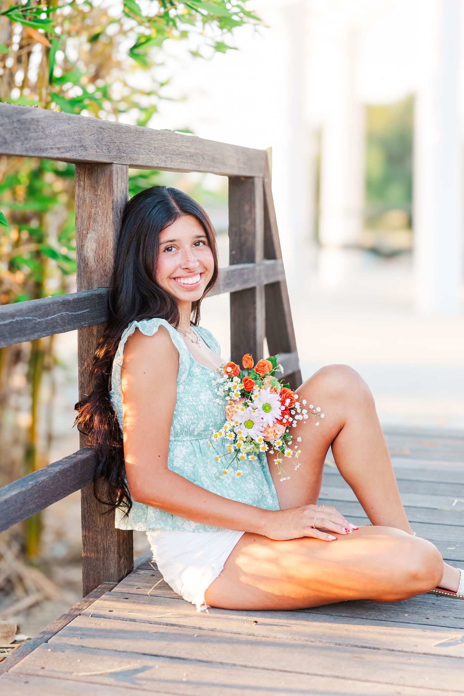 A person in a mint green dress sits outdoors holding a colorful bouquet of wildflowers and baby's breath.