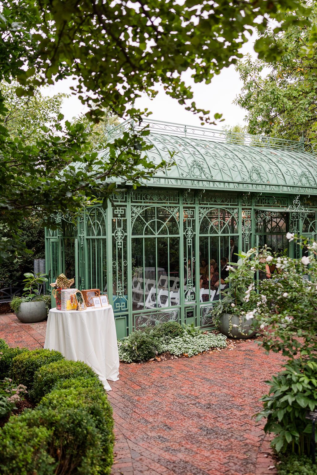 Elegant green conservatory with brick patio and white dining tables set for an upscale garden party reception.