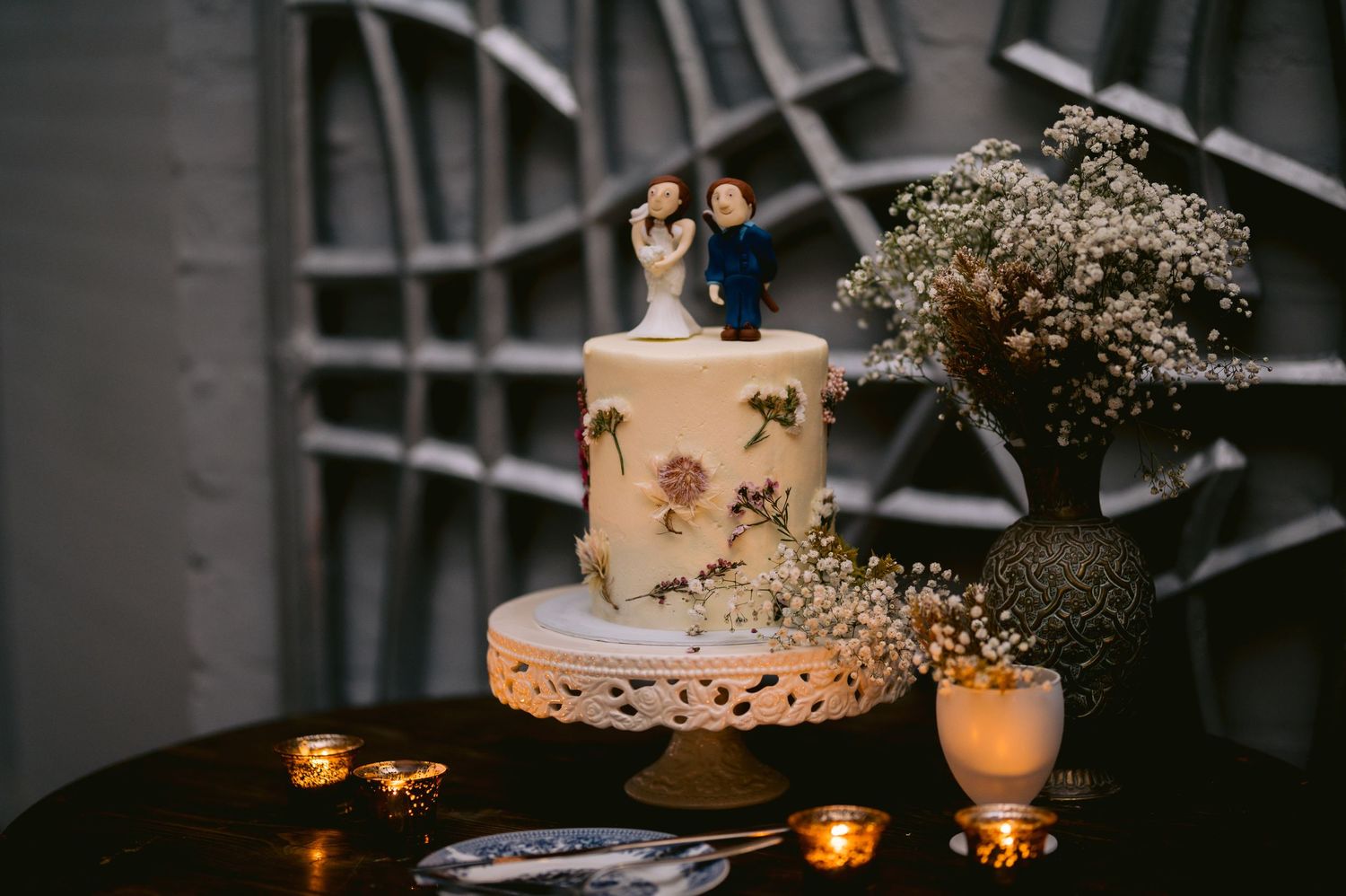 Elegant wedding cake display with candles and floral decorations on a rustic wooden table in a dimly lit venue.