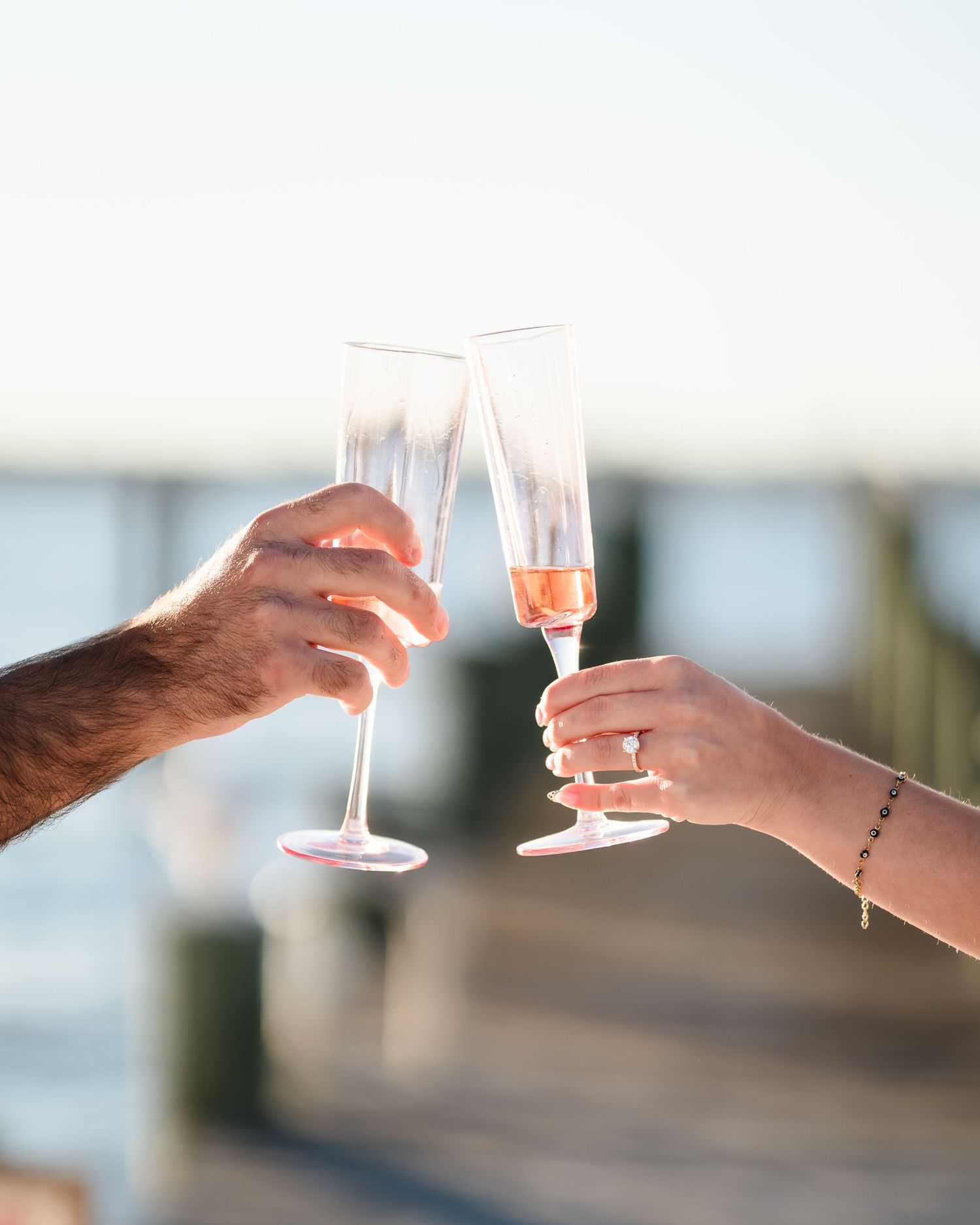 Hands toasting with champagne flutes against a waterfront backdrop.
