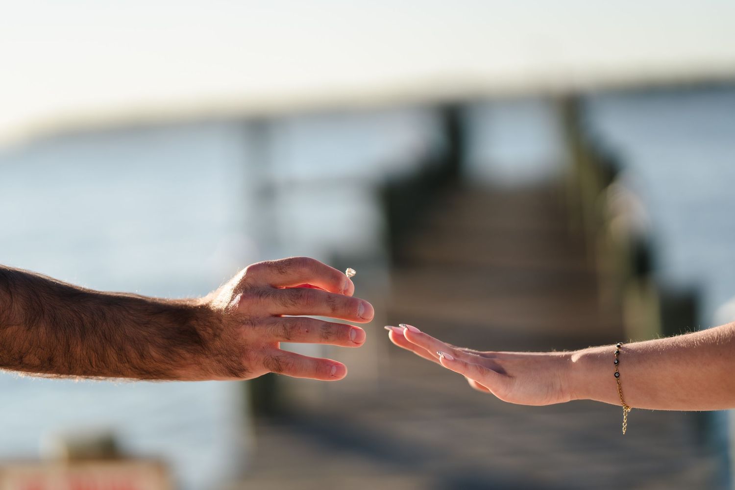 A couple holds hands against a sunset backdrop at a waterfront location.