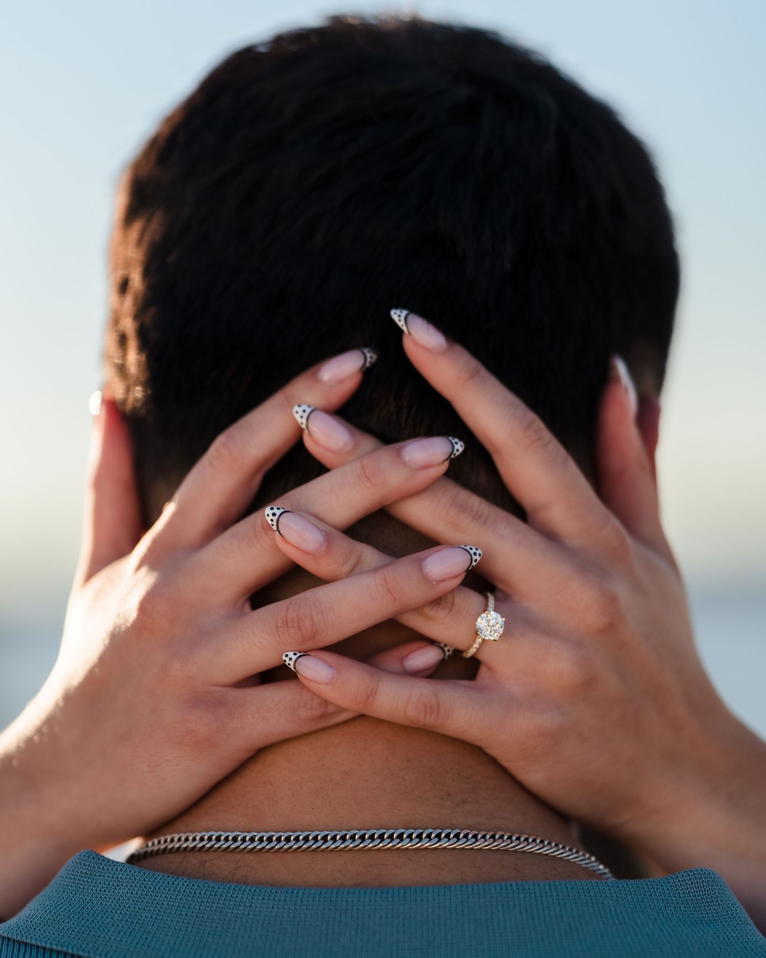 Close-up of hands displaying engagement rings against a blurred background.