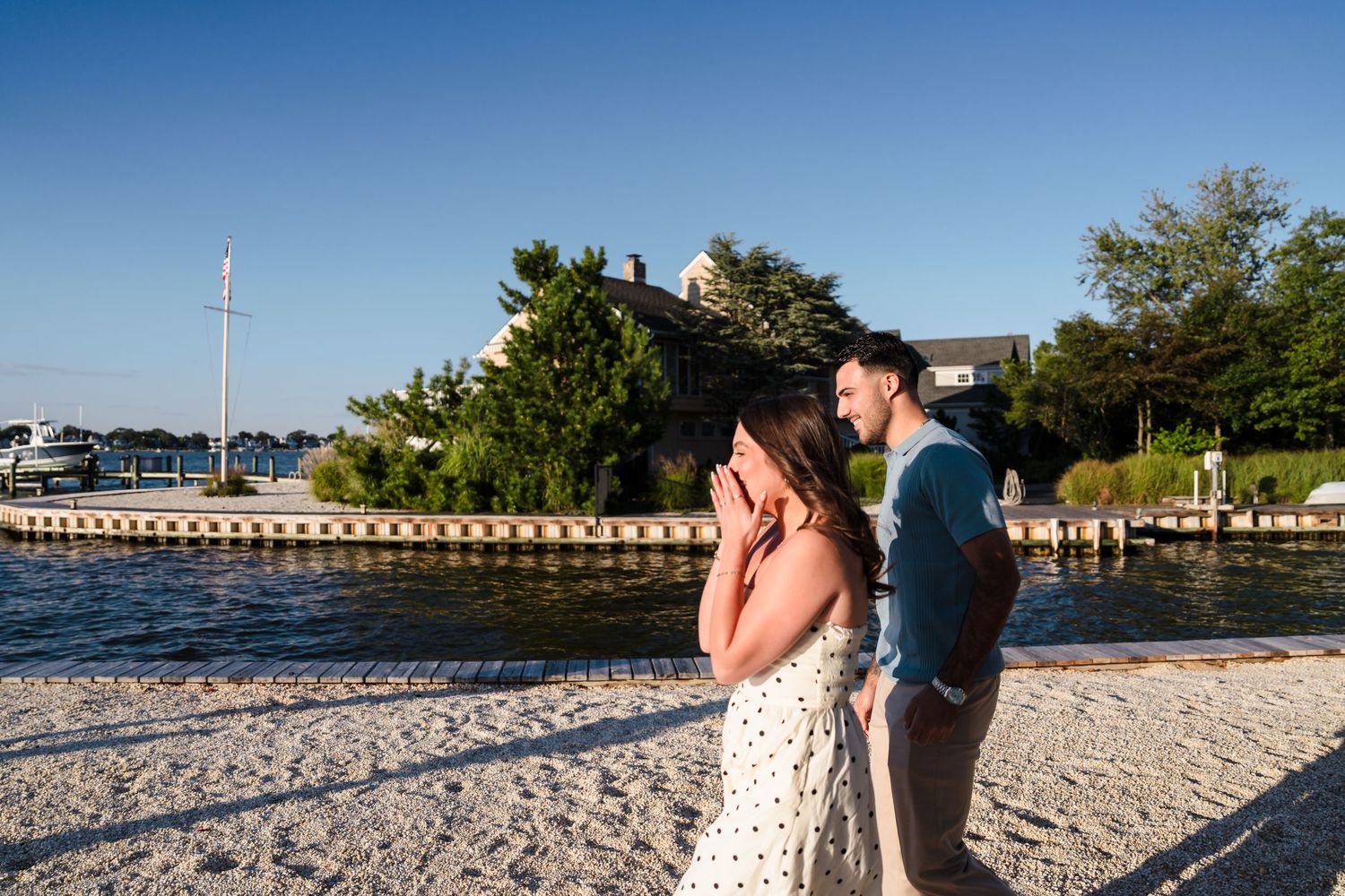 Couple walking along a scenic beach with pier and blue water in the background.