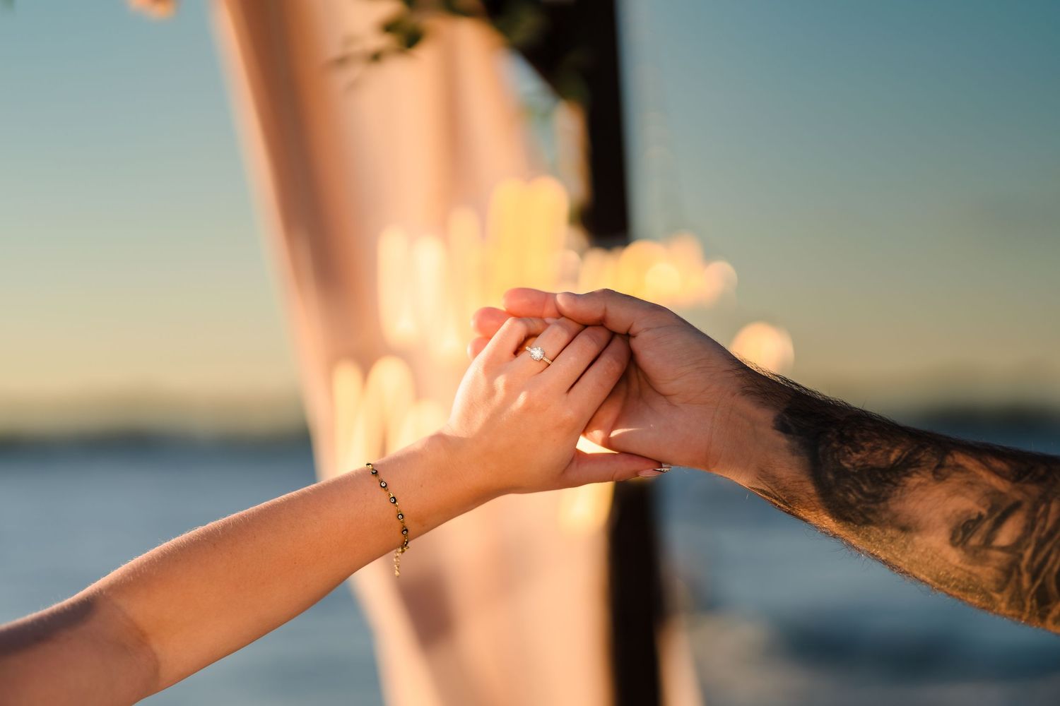 A romantic couple shares an intimate moment on a dock at sunset with sparkling water in the background.