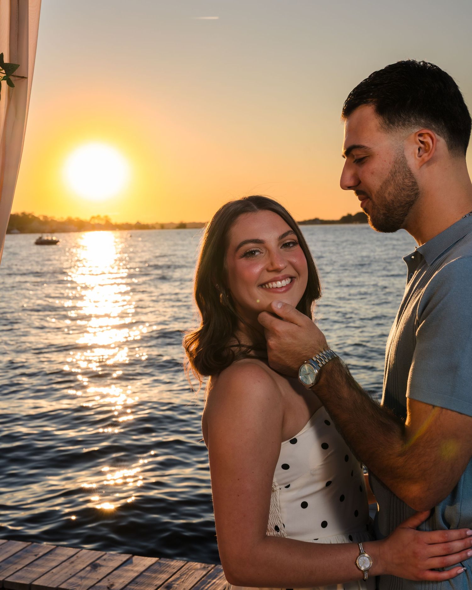 A couple shares a tender moment on a wooden dock during golden hour by the ocean.