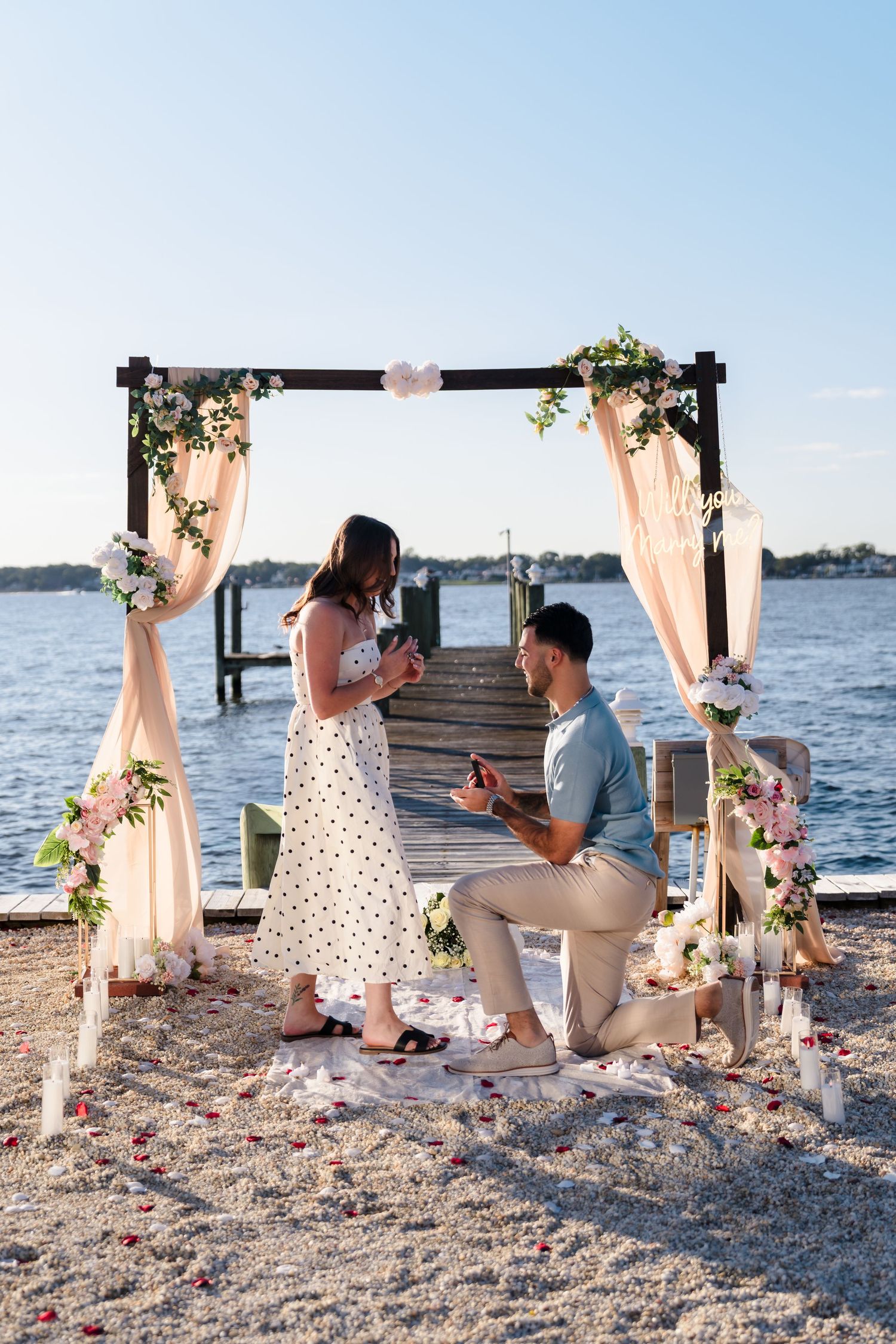 Couple sharing a special moment under a floral-decorated arch by the ocean during a proposal.