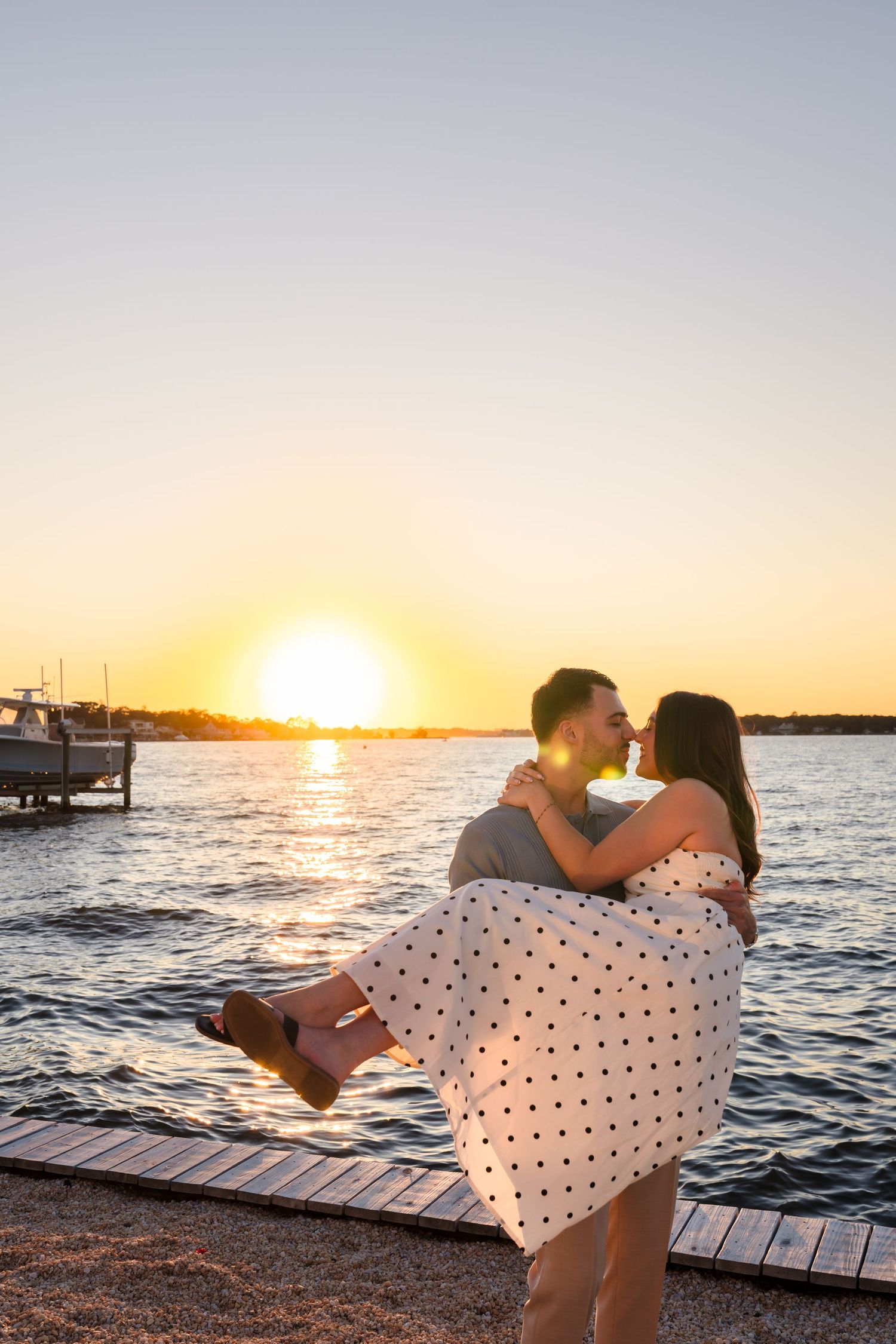 Romantic sunset photoshoot on a dock showing playful dip pose over water.