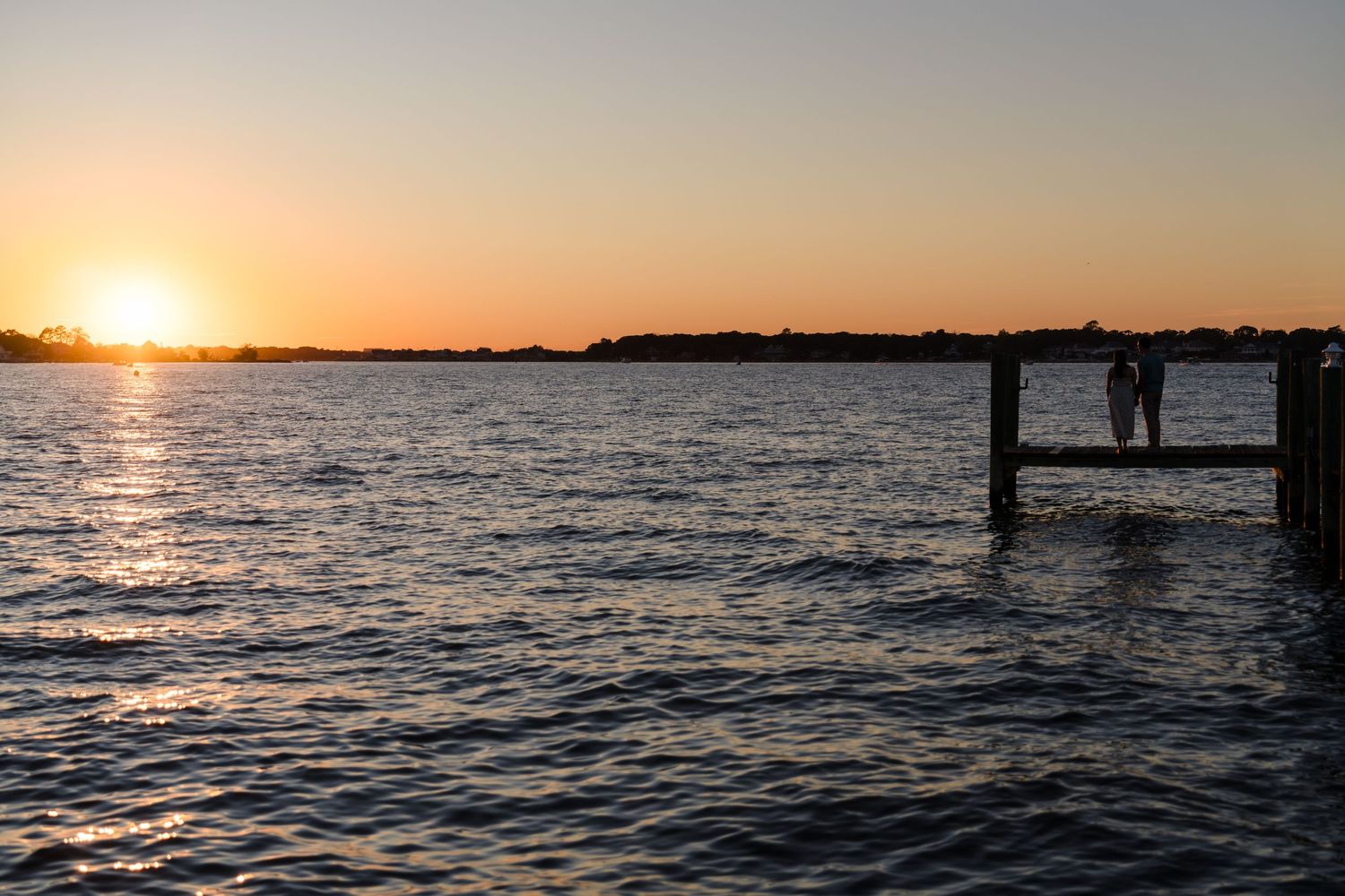 Panoramic sunset view over calm waters with dock silhouettes.