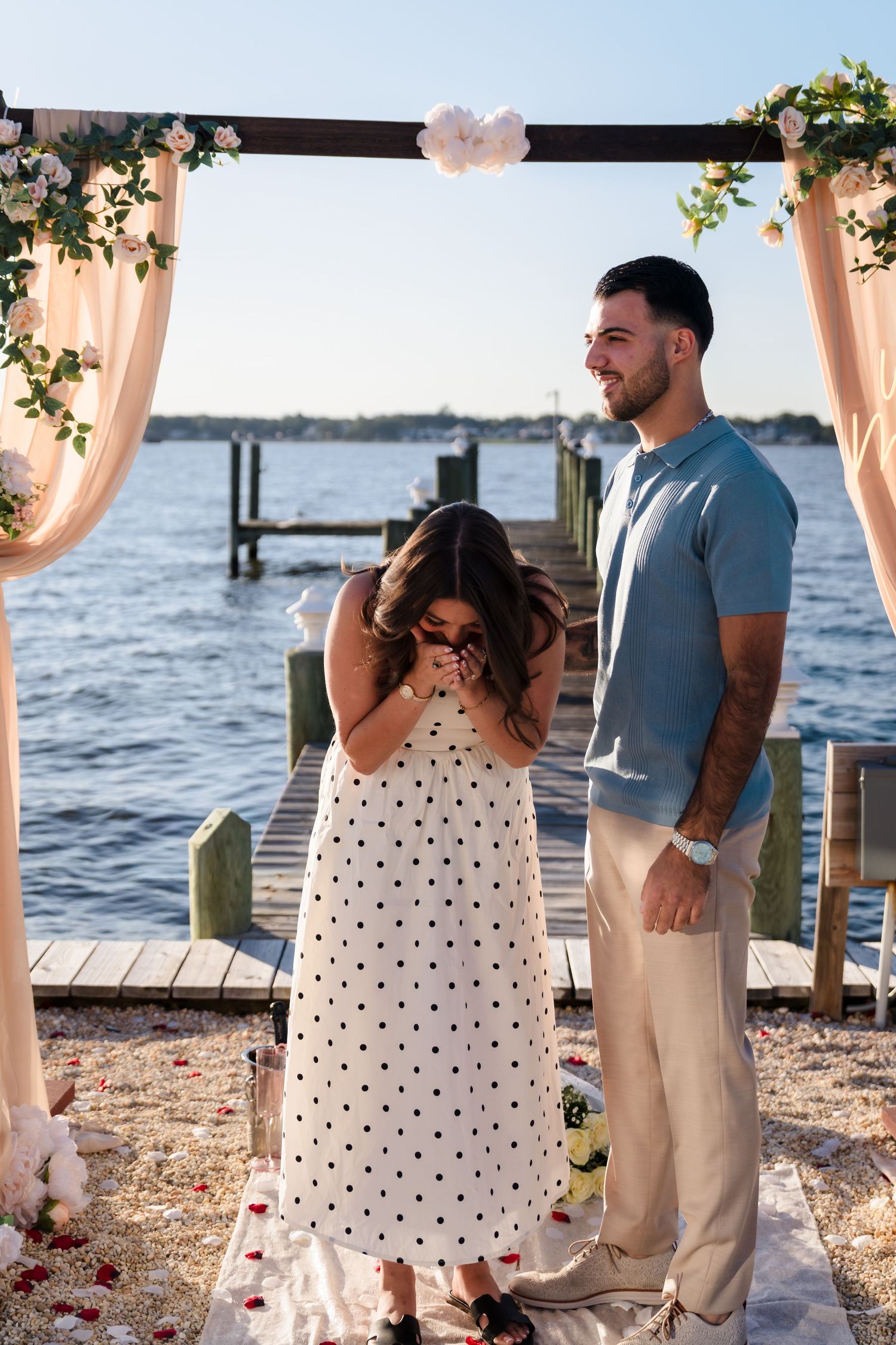 Candid moments of a beach proposal with polka dot dress and khaki attire by the water.