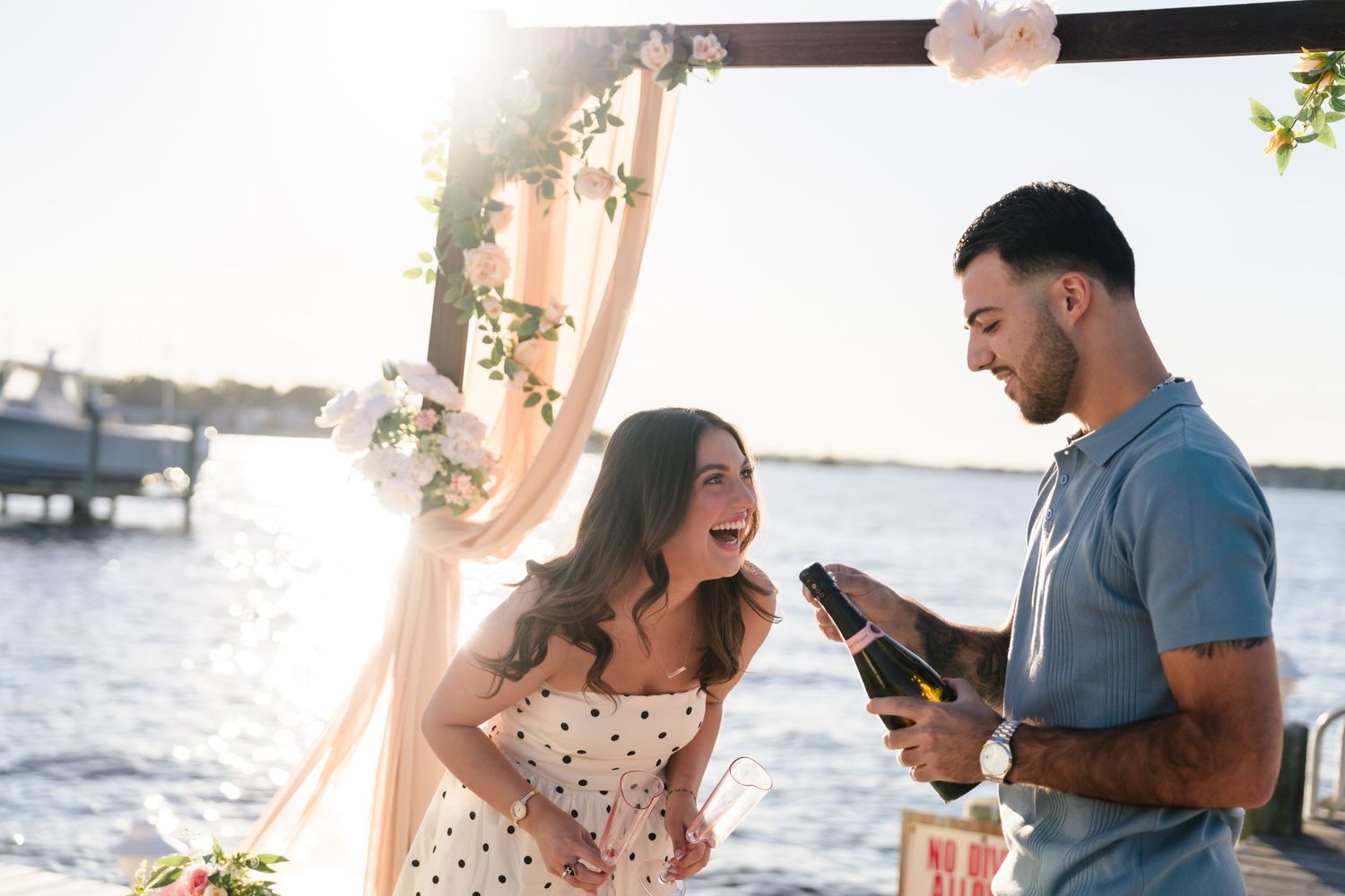 Romantic seaside proposal with decorated arch and rose petals on sandy beach.