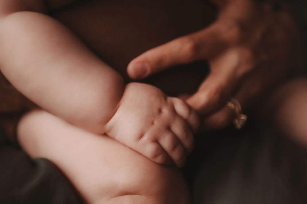 Close-up photo of two hands gently touching and intertwining fingers against a dark background.