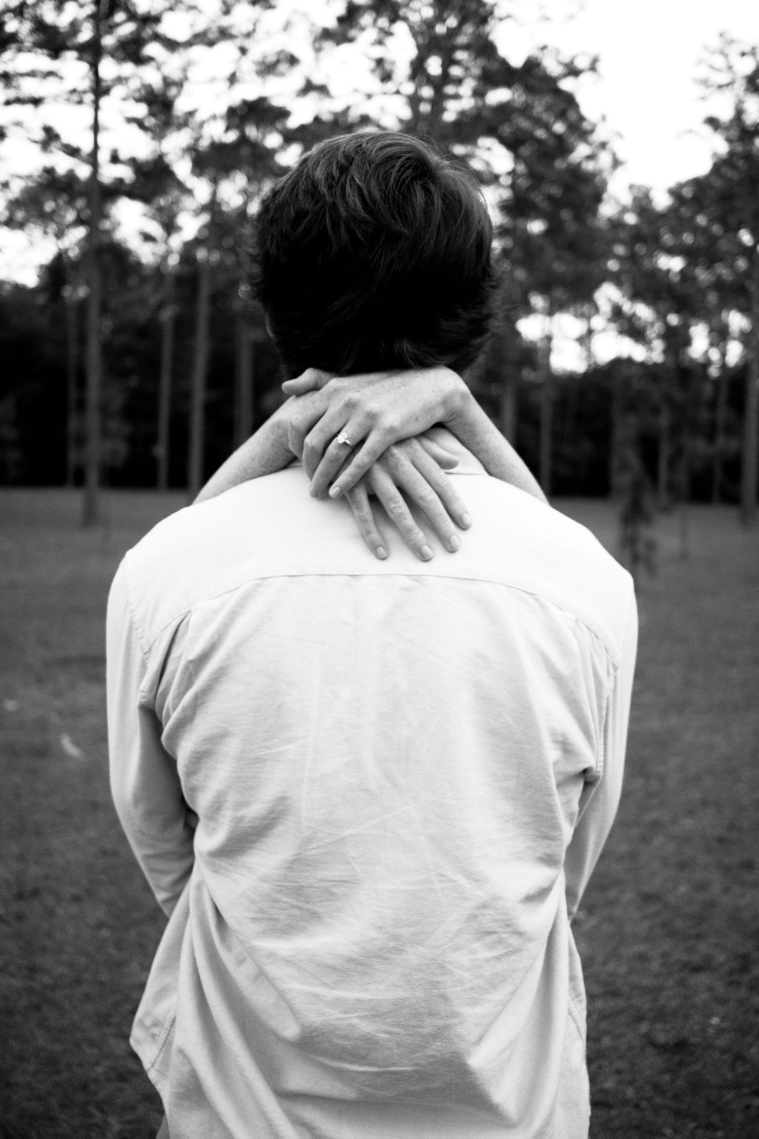 Black and white photo showing the back view of someone in white with a hand resting on their shoulder.