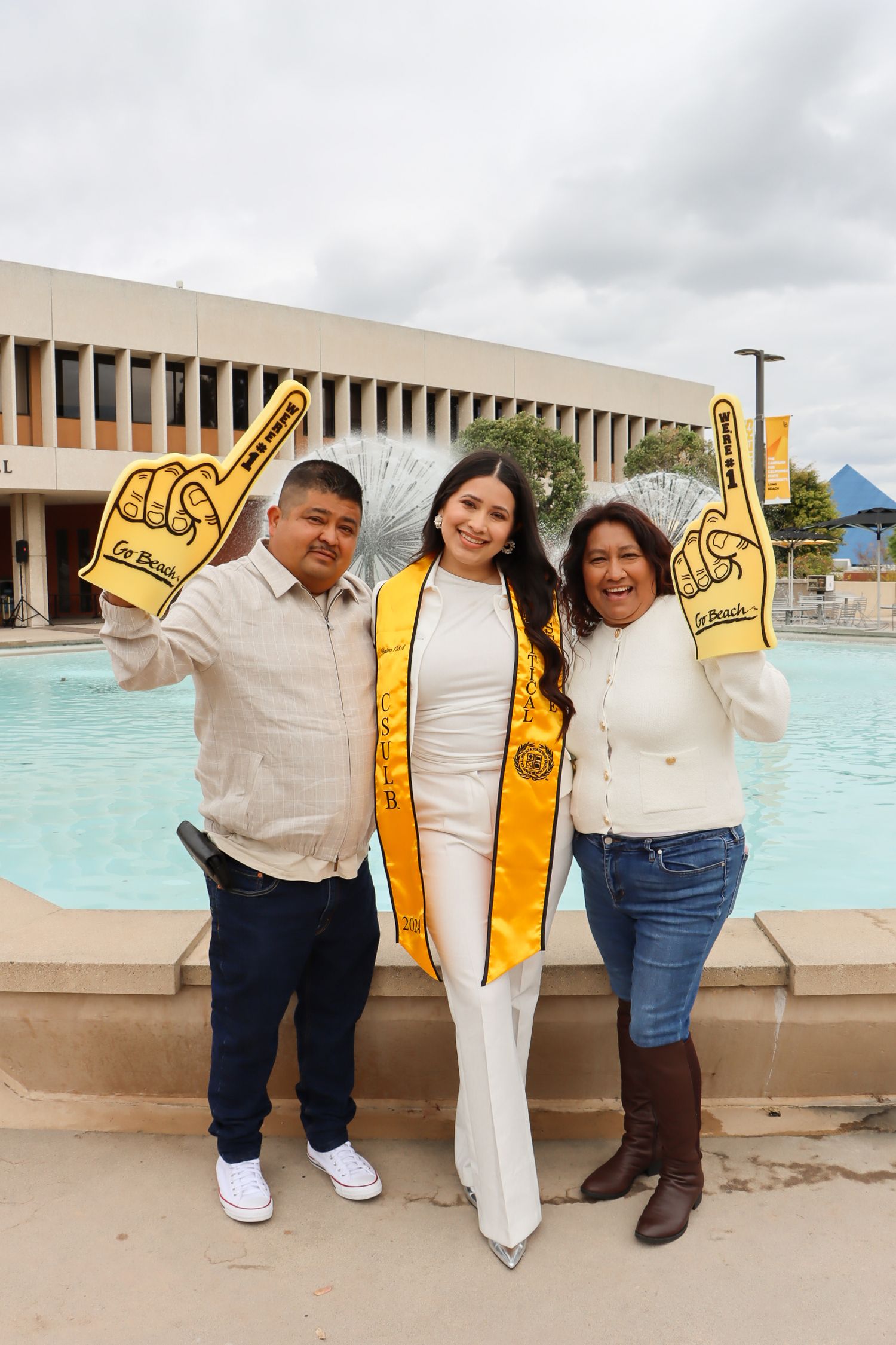 Group poses with yellow graduation stoles in front of campus fountain.