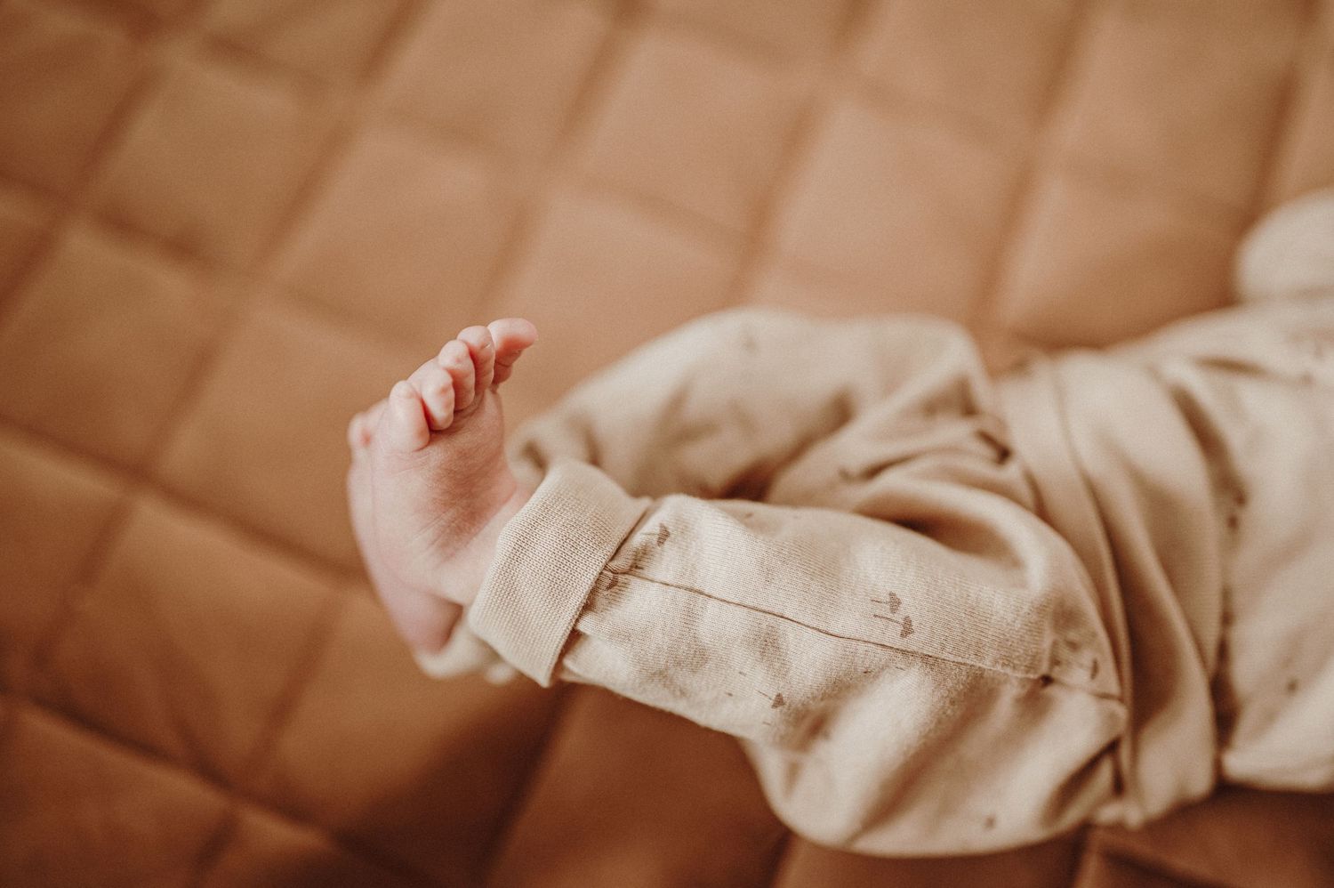 Close-up of infant's arm against quilted beige fabric background.
