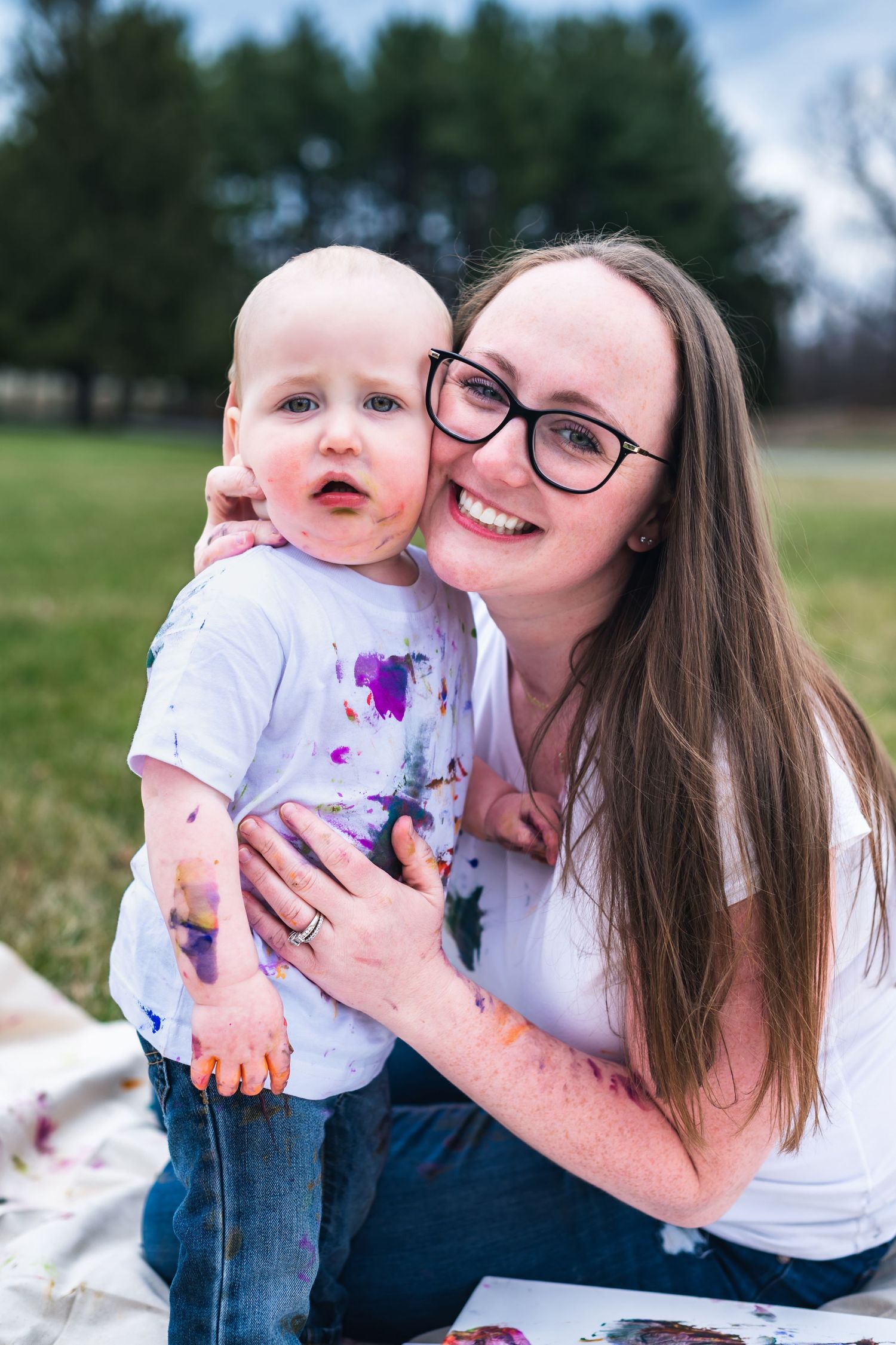 Parent and baby covered in paint sharing a special messy art moment outdoors.
