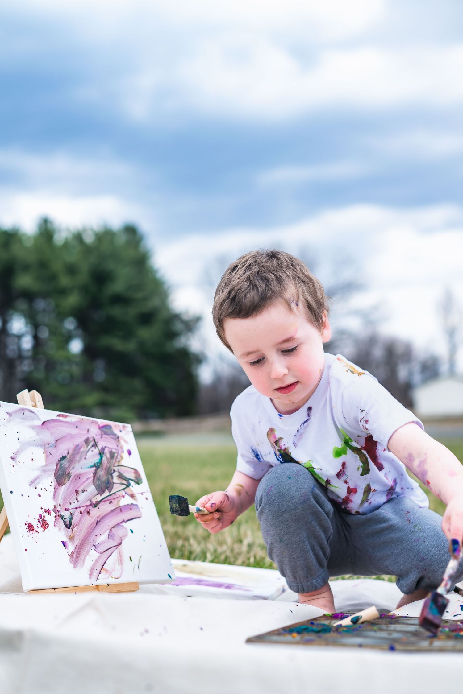 A child crouches down to create colorful paint art outside on a bright spring day.