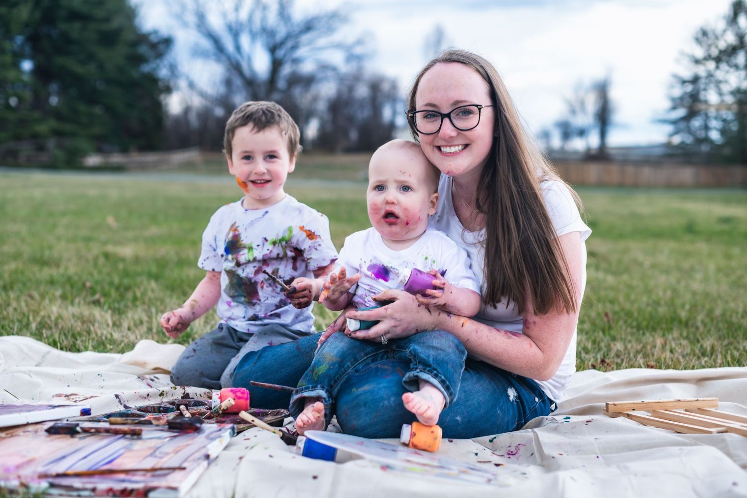 A family enjoys a picnic outdoors together on a blanket in a grassy field during a spring afternoon.