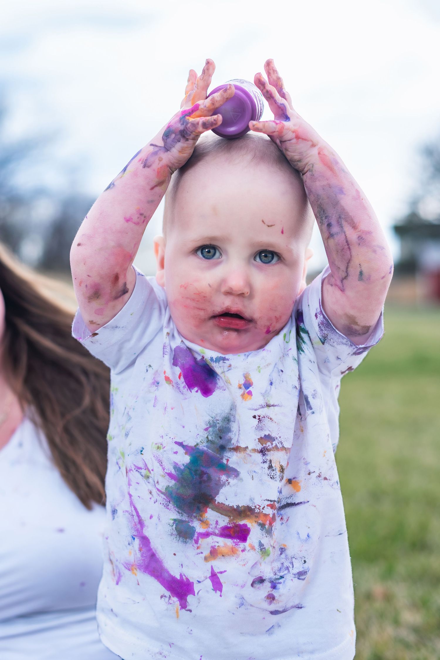 Paint-covered white shirt shows evidence of messy creative play outdoors with colorful splatters and stains.