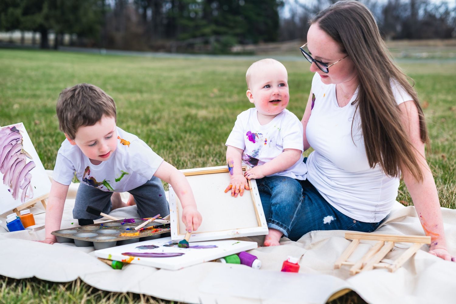 A fun art activity unfolds on a blanket in a grassy field with colorful art supplies spread out.