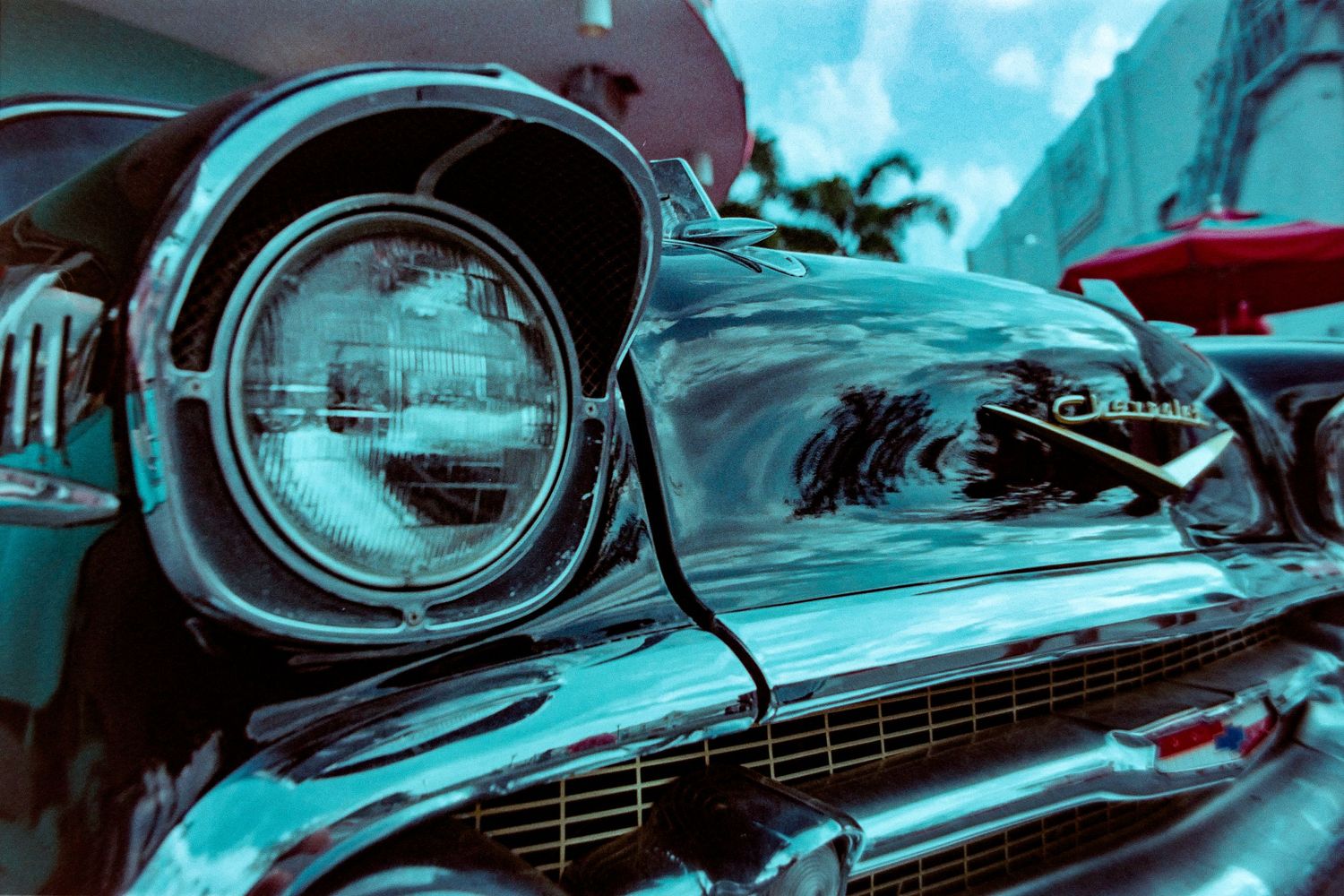 Close-up view of a classic Chevrolet car headlight and chrome grille in vibrant turquoise tones.