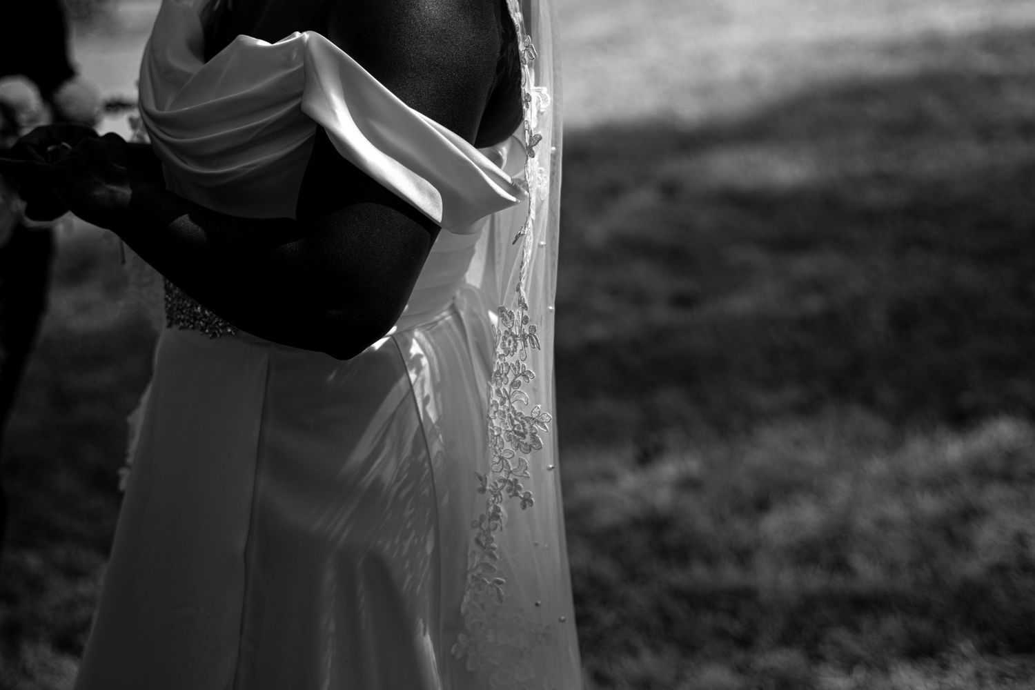 Artistic black and white photograph of a wedding dress detail with flowing veil.