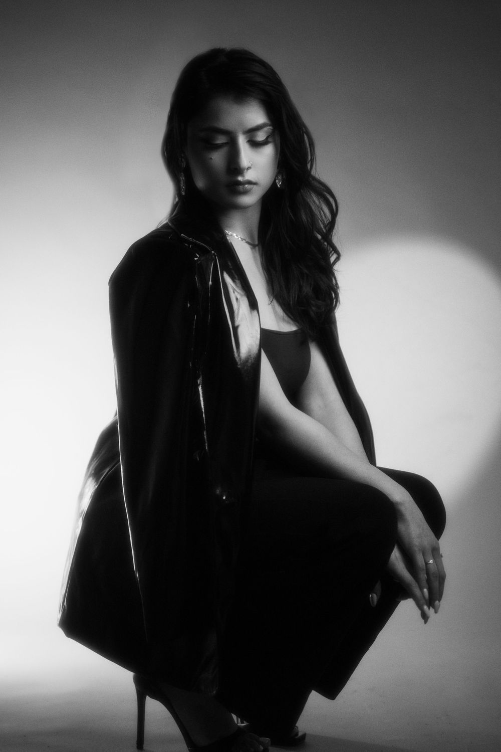 Dramatic black and white portrait of someone posing in dark clothing with long flowing hair against light background.