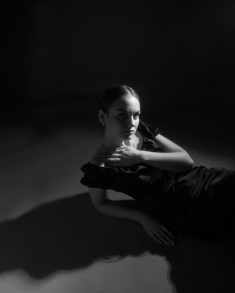 A dramatic black and white portrait showing a figure in elegant shadows with reflective surfaces creating artistic contrast.
