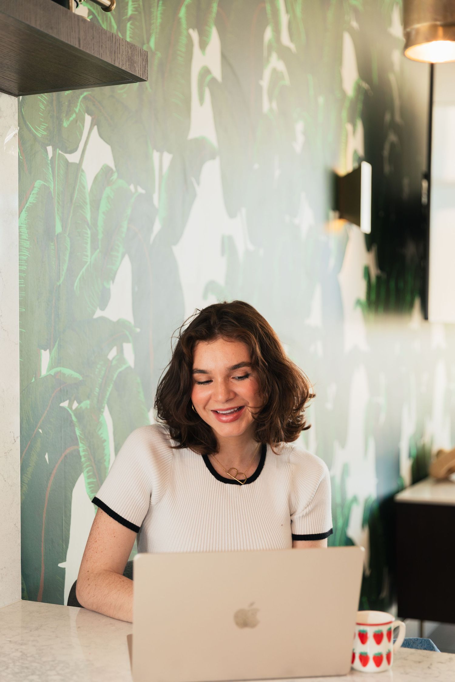 Person working at a laptop in a bright room with green patterned wallpaper.
