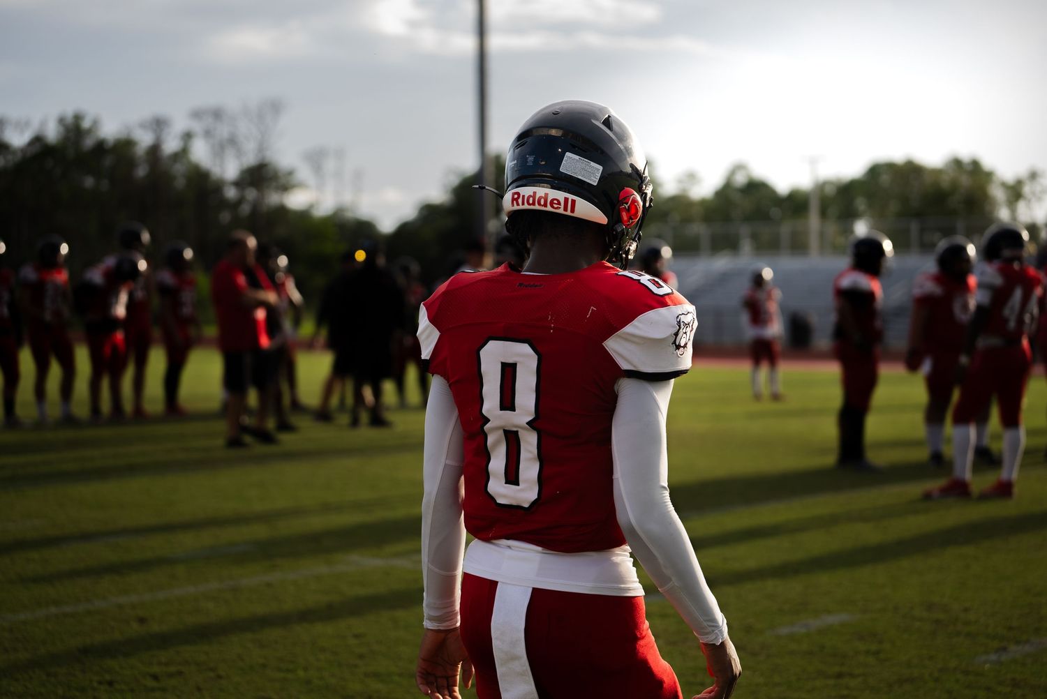 Football player in red jersey numbered 8 stands on practice field at dusk.