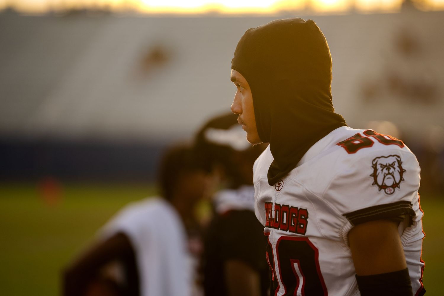 Football player wearing a beanie and jersey stands on field at sunset.