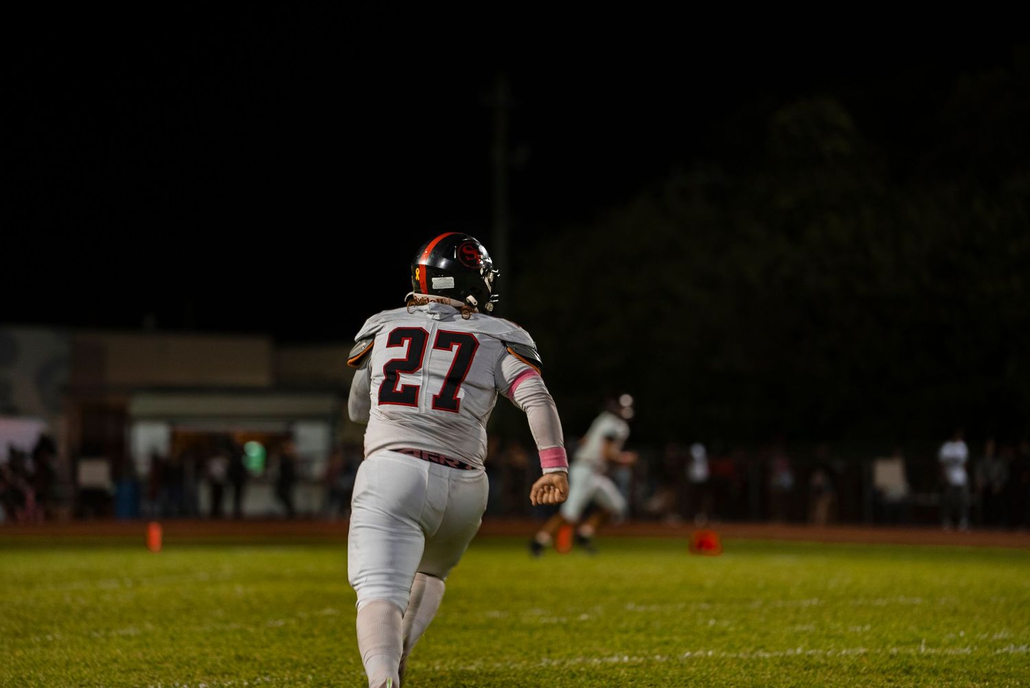 Football player in white jersey number 27 running on illuminated field at night.