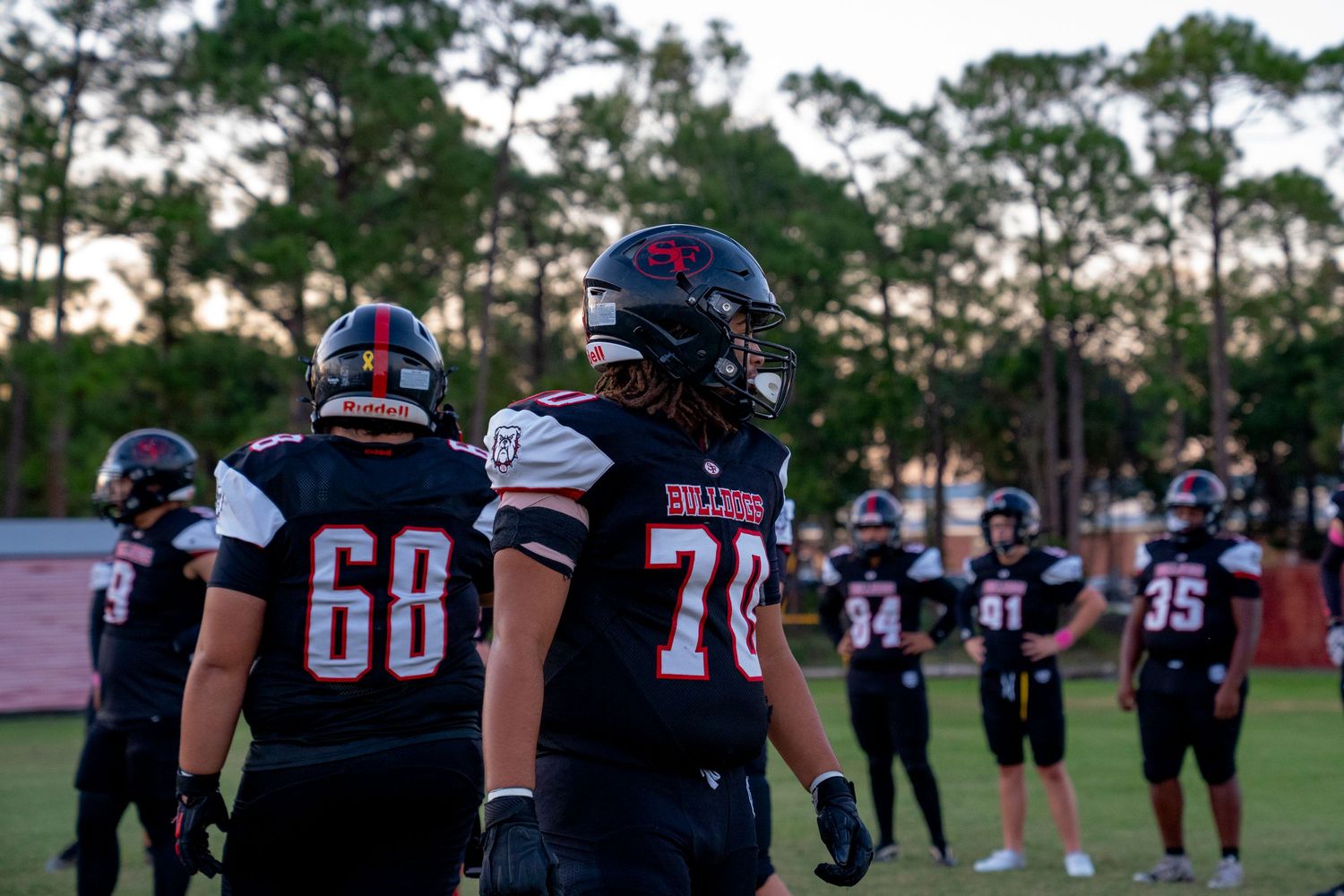 Football players in navy uniforms standing on field at sunset with jersey numbers visible.