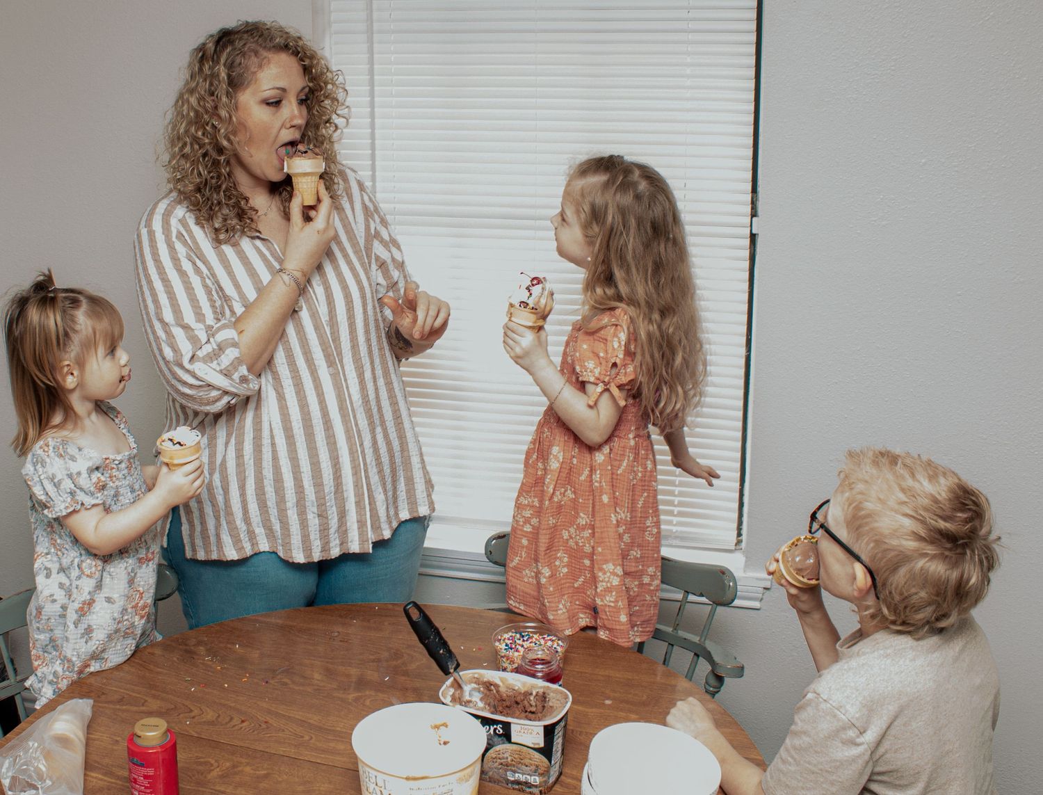 A group enjoying ice cream cones together around a wooden table with various dessert toppings and treats.