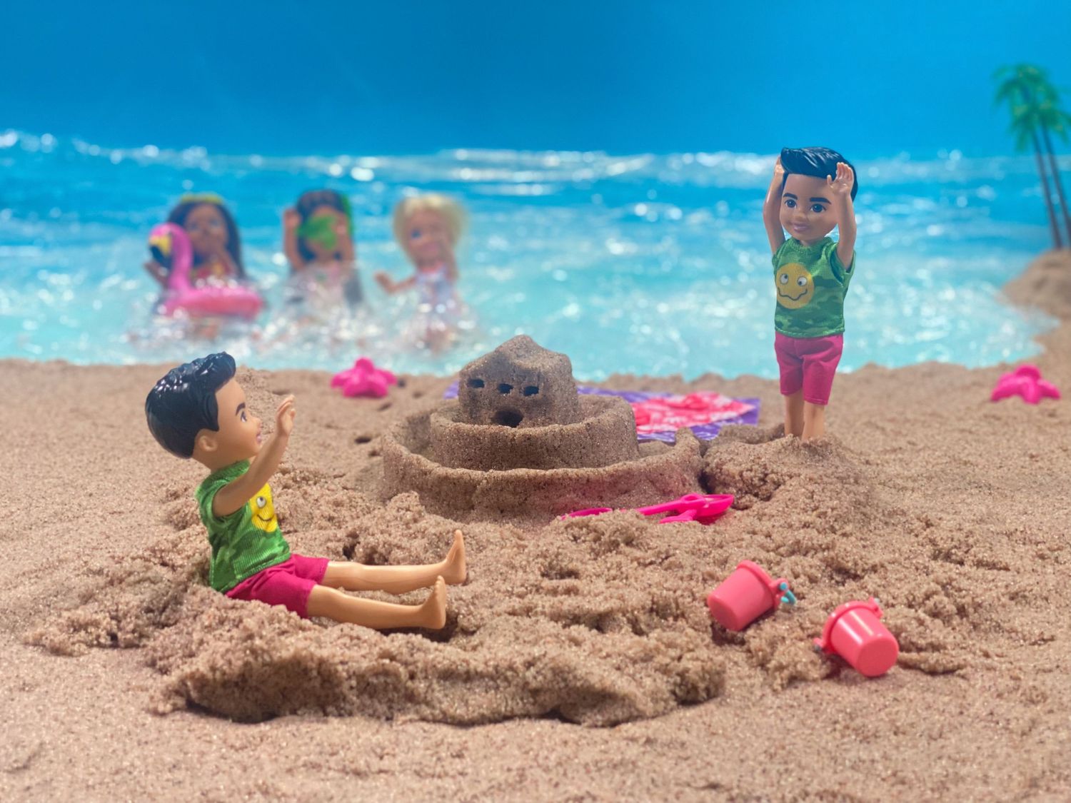 Children playing at a tropical beach with sand castles and pink toys while others swim in the turquoise ocean.
