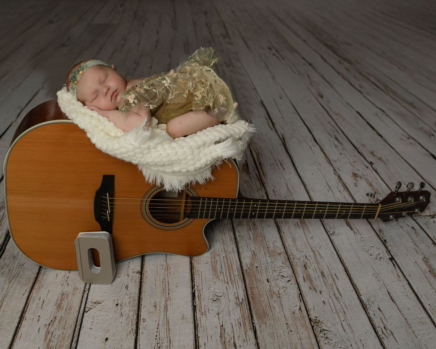 A peaceful baby sleeps on a white blanket draped over an acoustic guitar on wooden floor.
