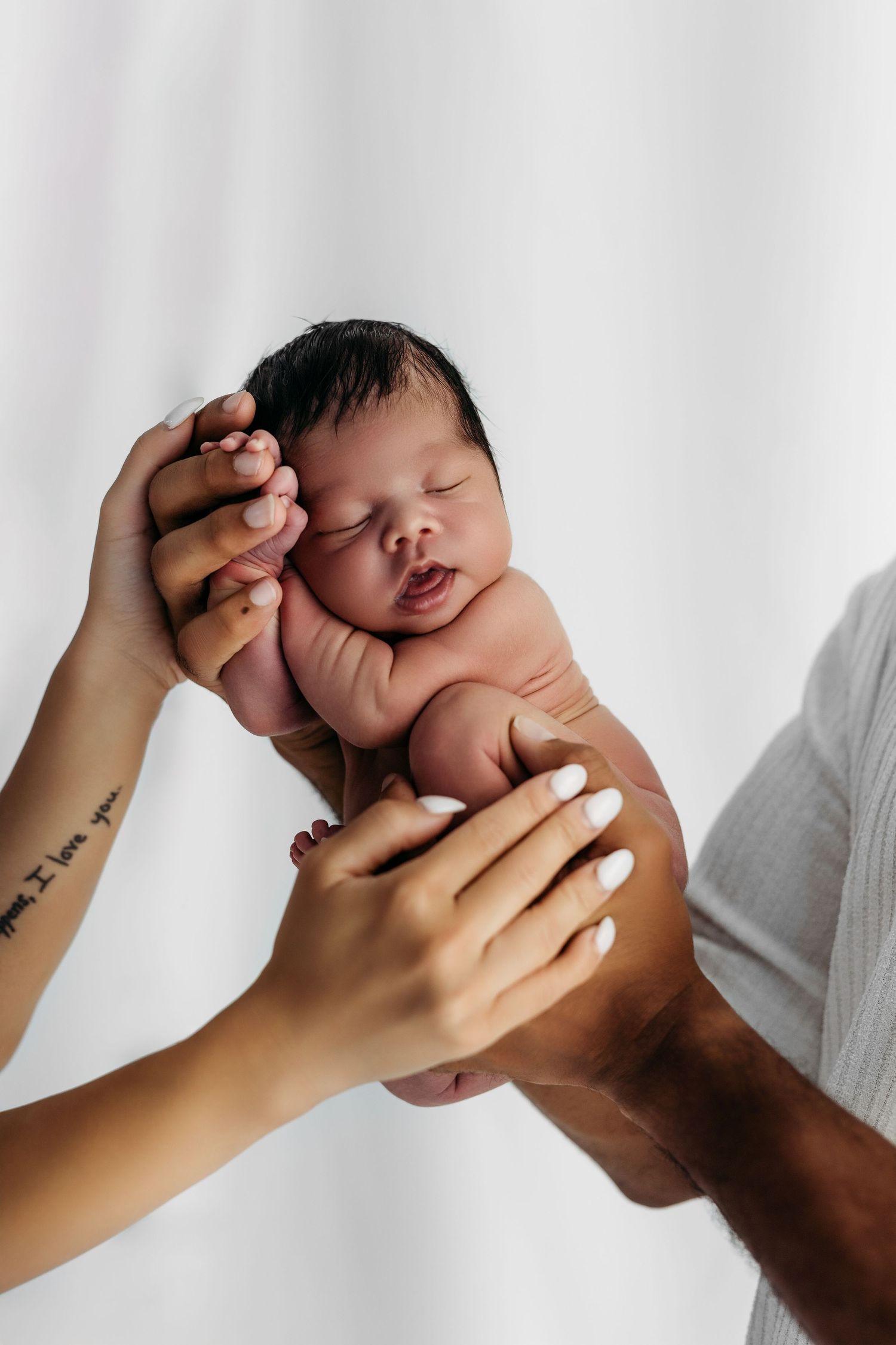 Gentle hands support a peaceful sleeping newborn baby against a white background during a tender portrait session.