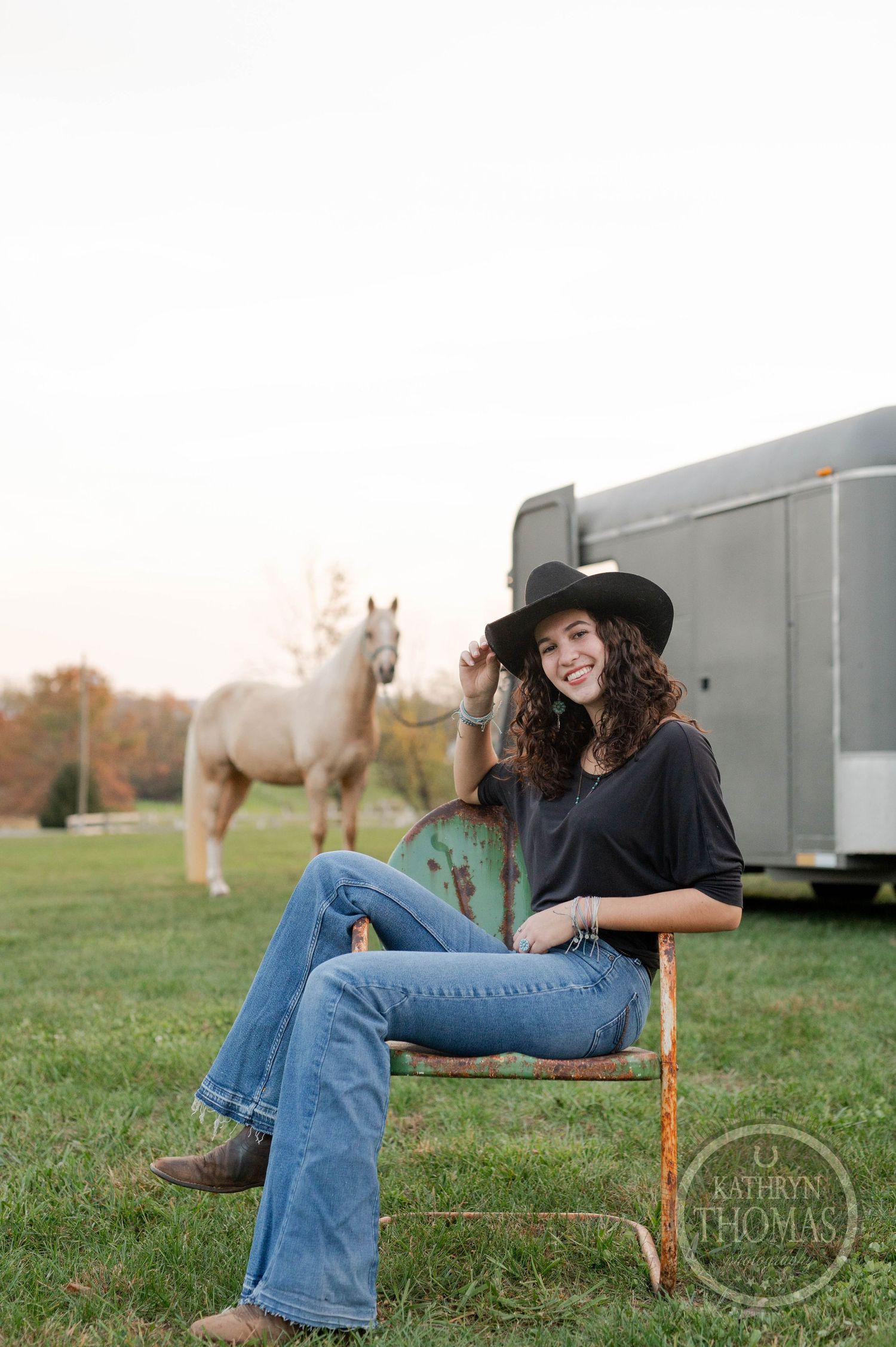 Casual outdoor portrait with a white horse and silver trailer in the background during golden hour.
