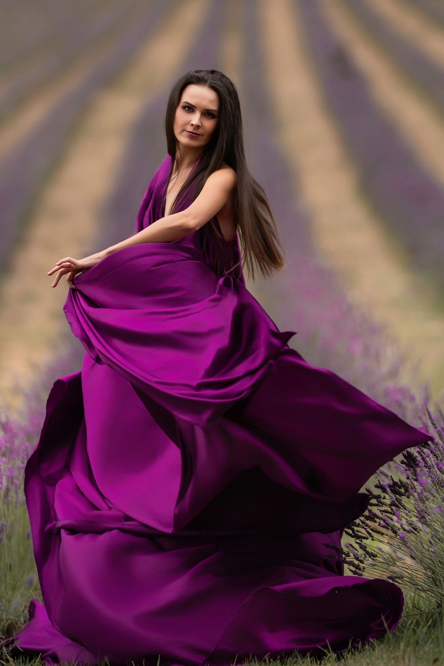 A flowing purple gown billows dramatically in a lavender field during a dreamy outdoor photo session.
