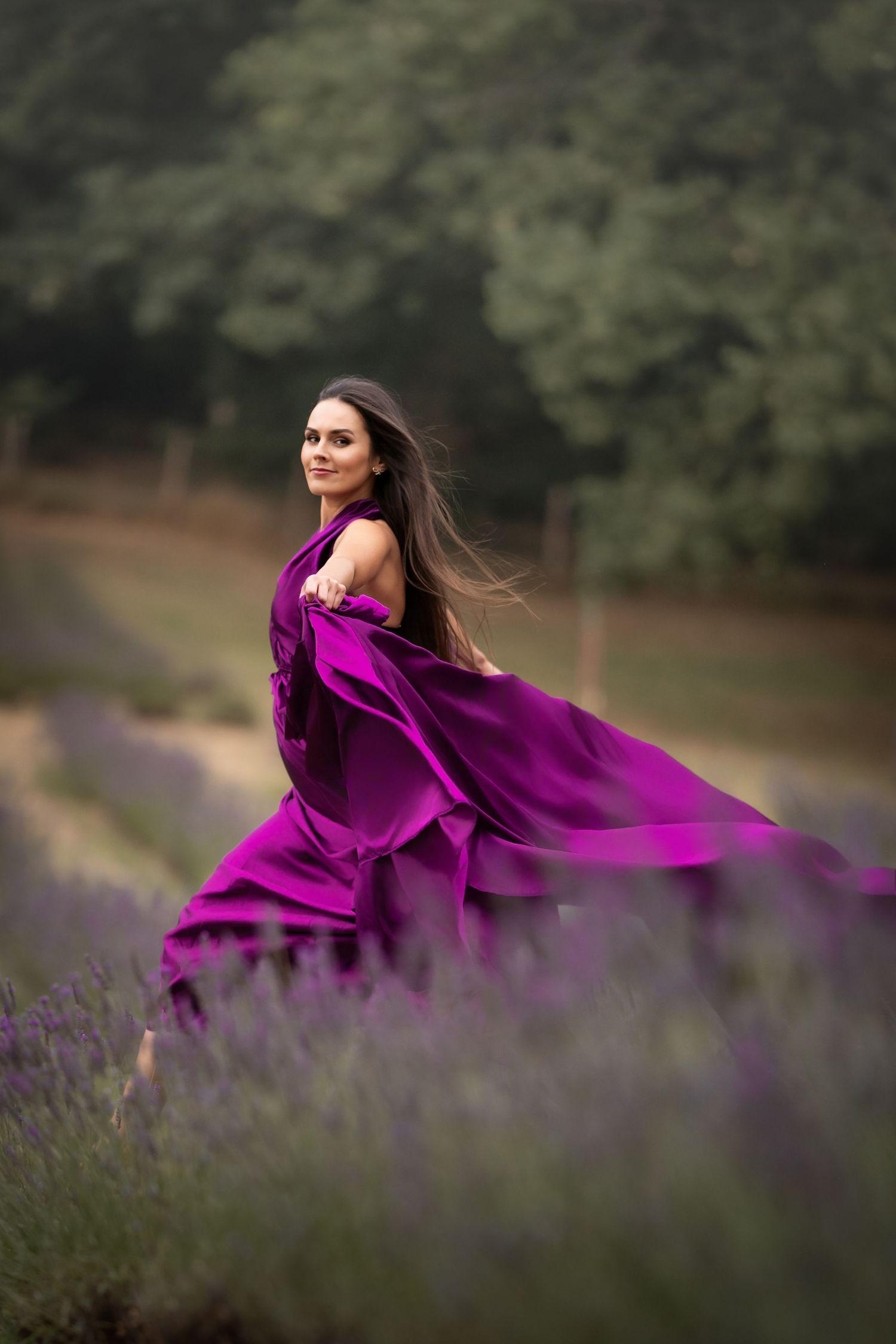 A flowing purple gown swirls dramatically in a lavender field during a dreamy outdoor photoshoot.