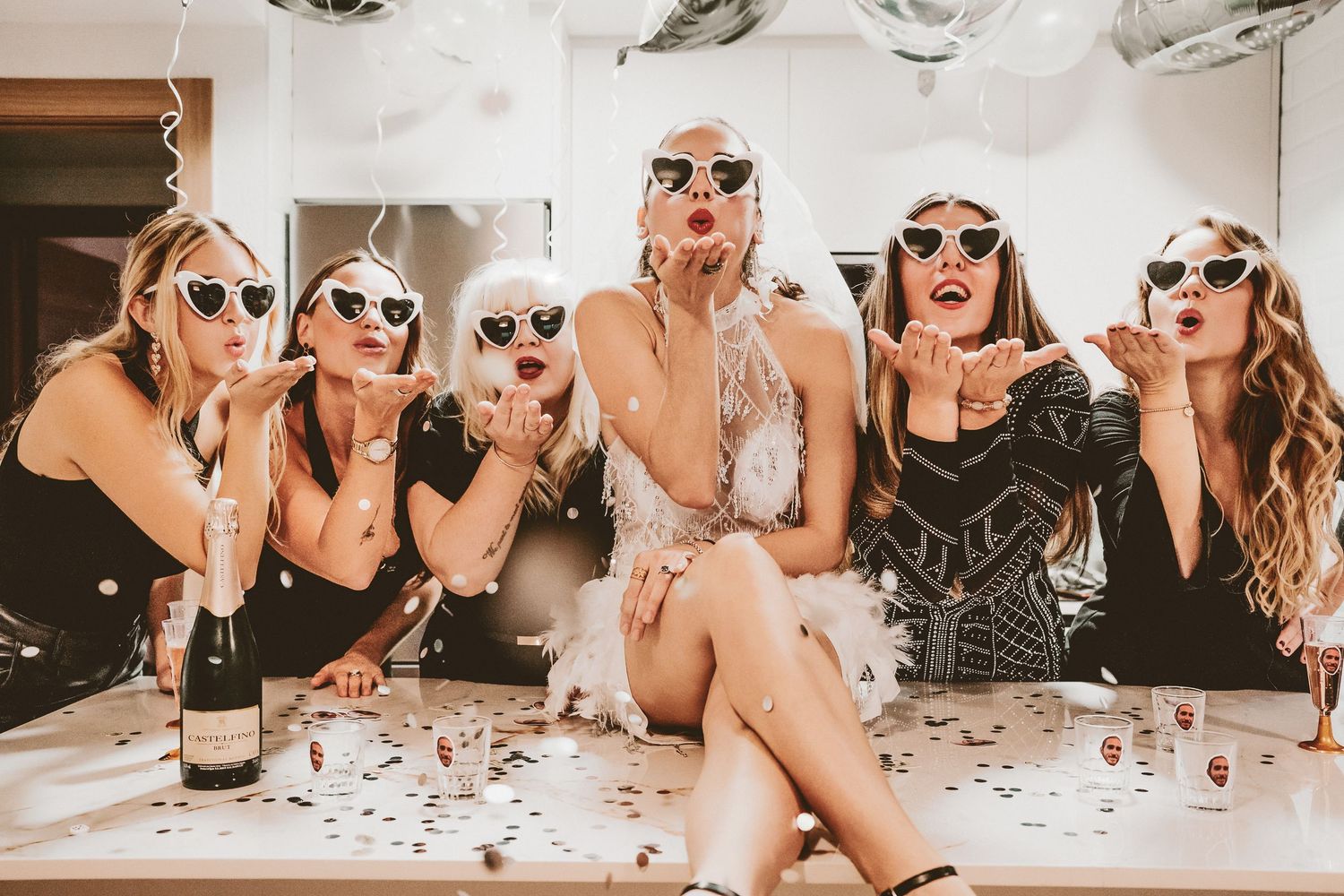 A group in matching white sunglasses poses together with confetti scattered on a white table during a celebration.