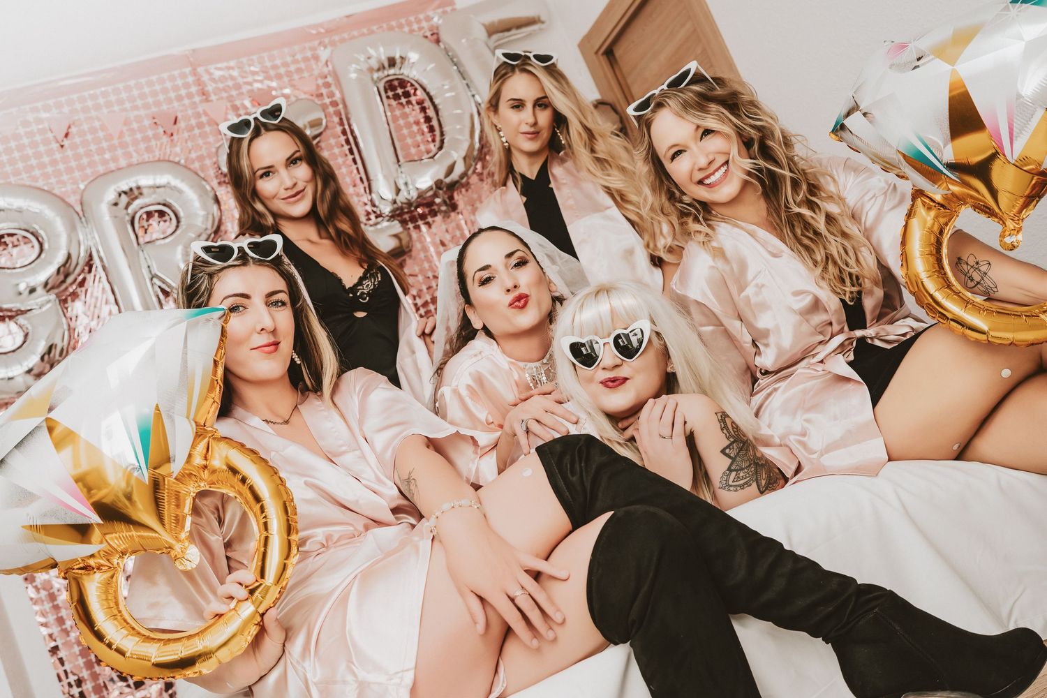 Group of friends celebrating with champagne and gold balloons at a festive pink-themed party.