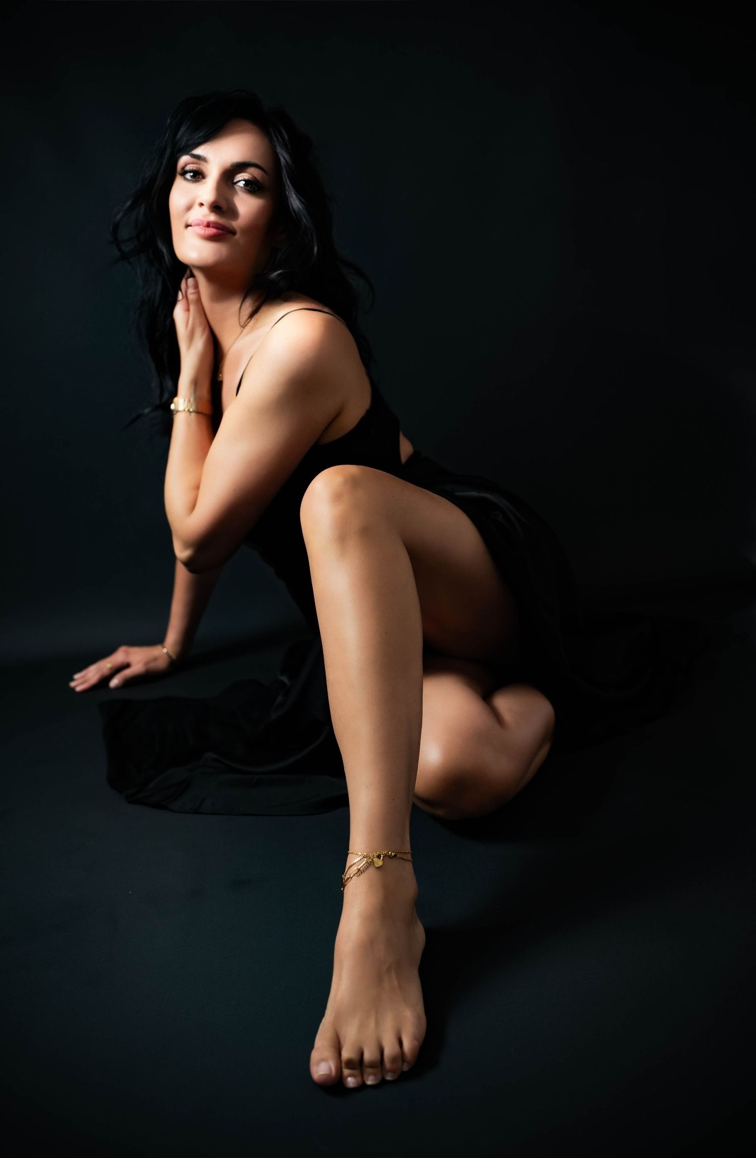 Artistic boudoir photo with dark background showing figure in black dress posing elegantly on floor.