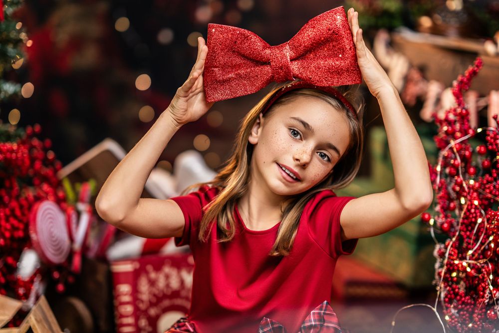 A festive holiday scene with red bows and decorative berries against a warm bokeh background.