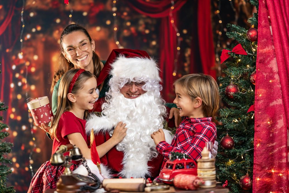 A festive holiday scene with children visiting Santa Claus in a decorated setting with red curtains and twinkling lights.